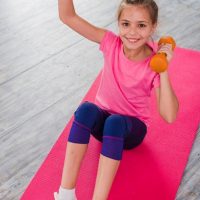 blonde girl sitting pink carpet exercising with dumbbell